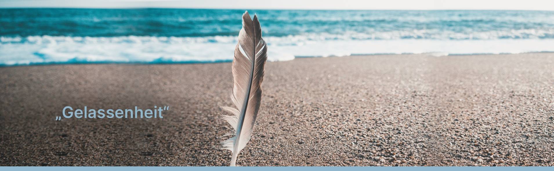 Zu sehen ist ein Strand aus der Froschperspektive. ImVordergrund steckt eine Vogelfeder im grobkörnigen Sand. Im Hintergrund ist türkisblaues Meer zu sehen, dessen kleine weiße Wellen an den Strand laufen.